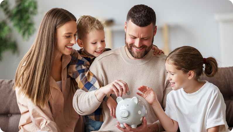 Family putting coins into a piggy bank, sitting together on a couch with smiles.
