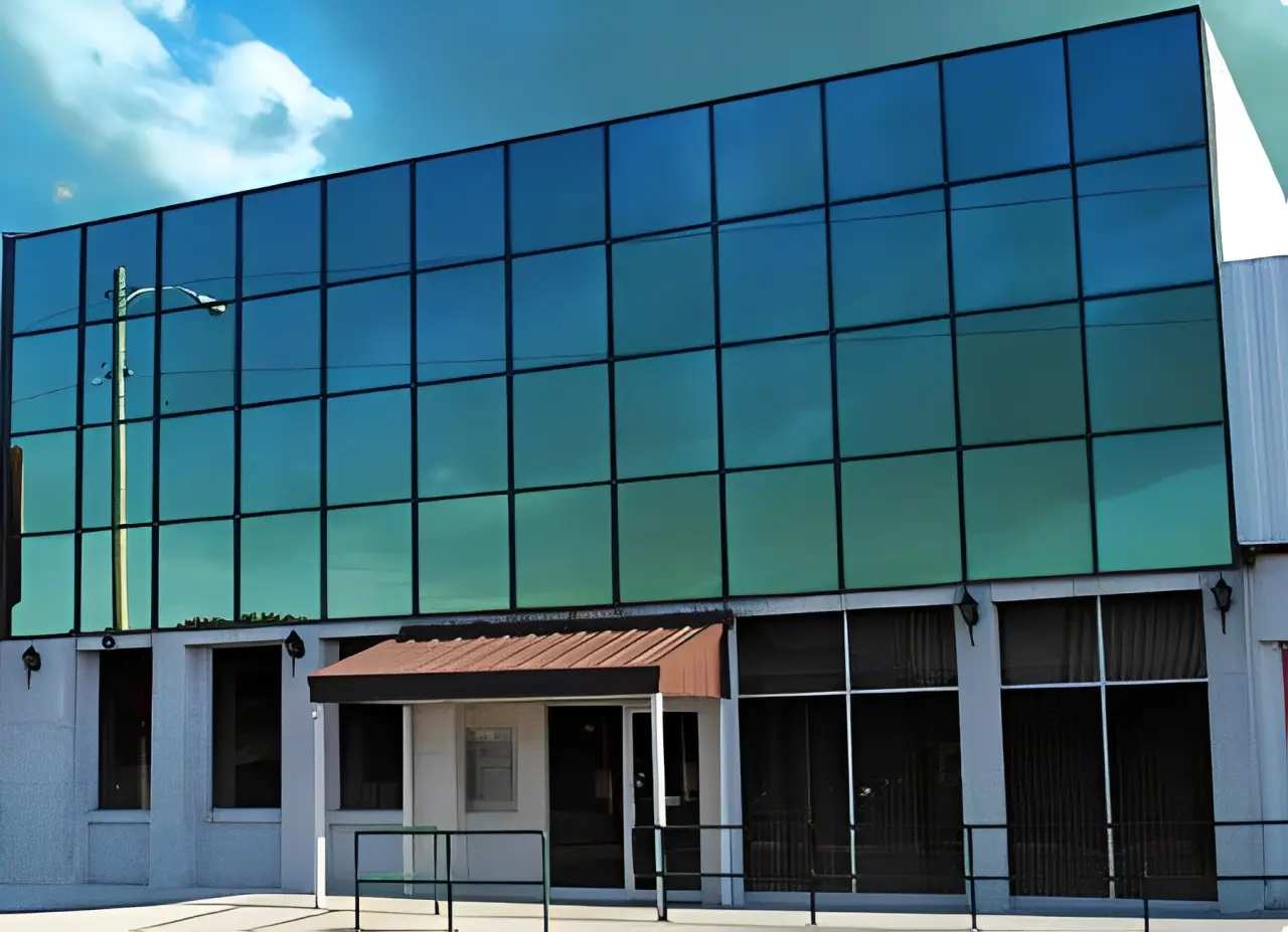 Glass-fronted building with a red awning over the entrance. The upper facade reflects the sky, while the lower section has small windows and a ramp.